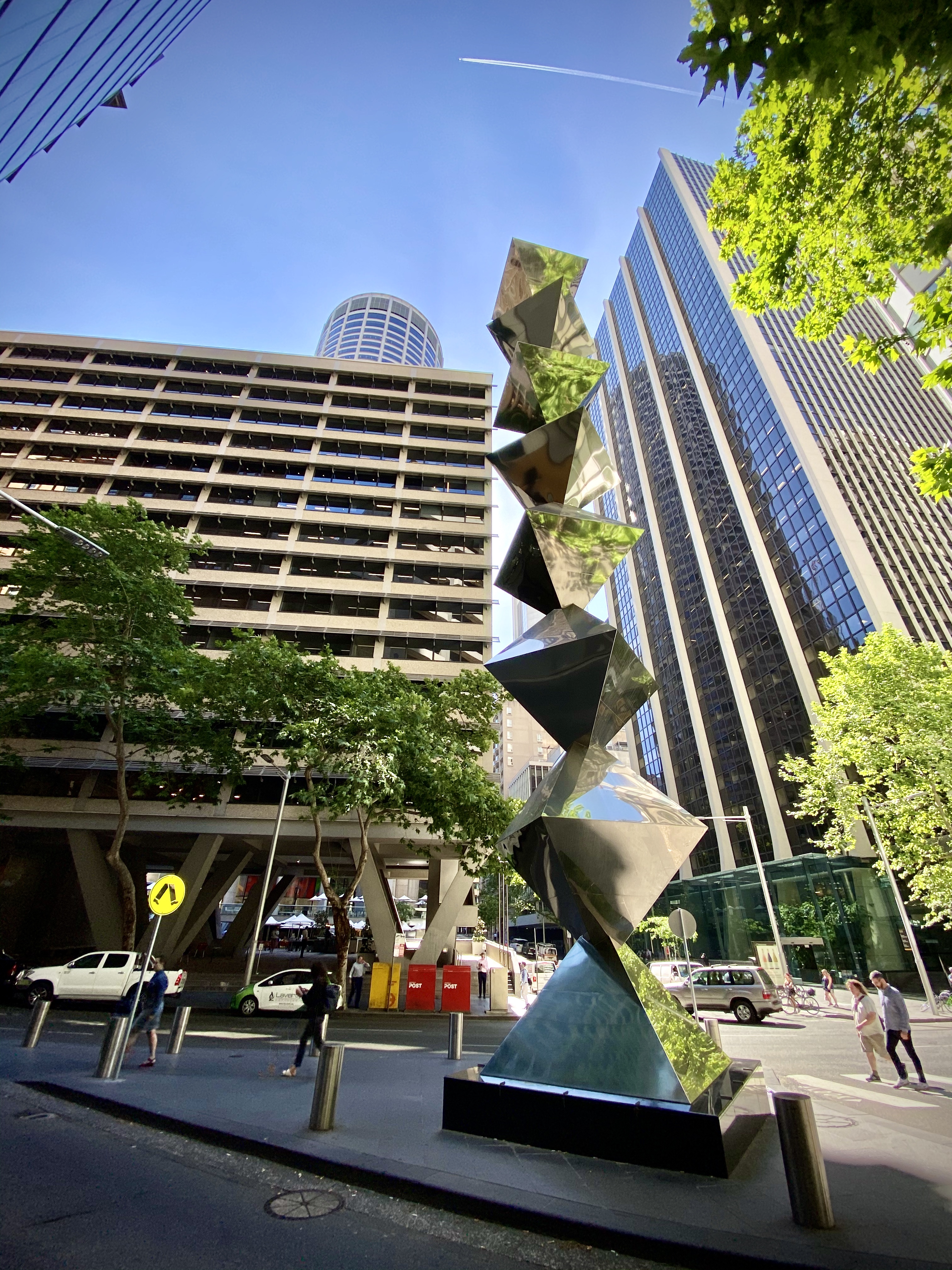 Looking up at the sky with an angular, reflective sculpture in the foreground and buildings in the background