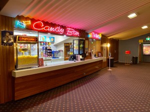 A counter with the sign candy bar and a popcorn machine under a sloping corrugated metal ceiling