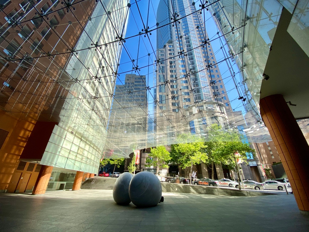 Looking up through a large glass awning with boulder-like sculptures in the foreground